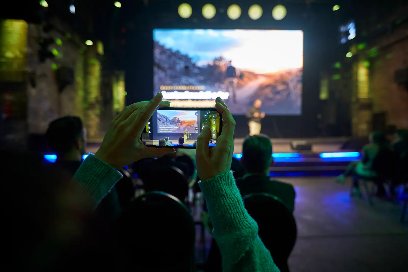Teilnehmende filmt mit dem Handy den Talk „Auslaufmodell oder Karrierebooster?“ auf der Bühne in DIE HALLE Tor 2